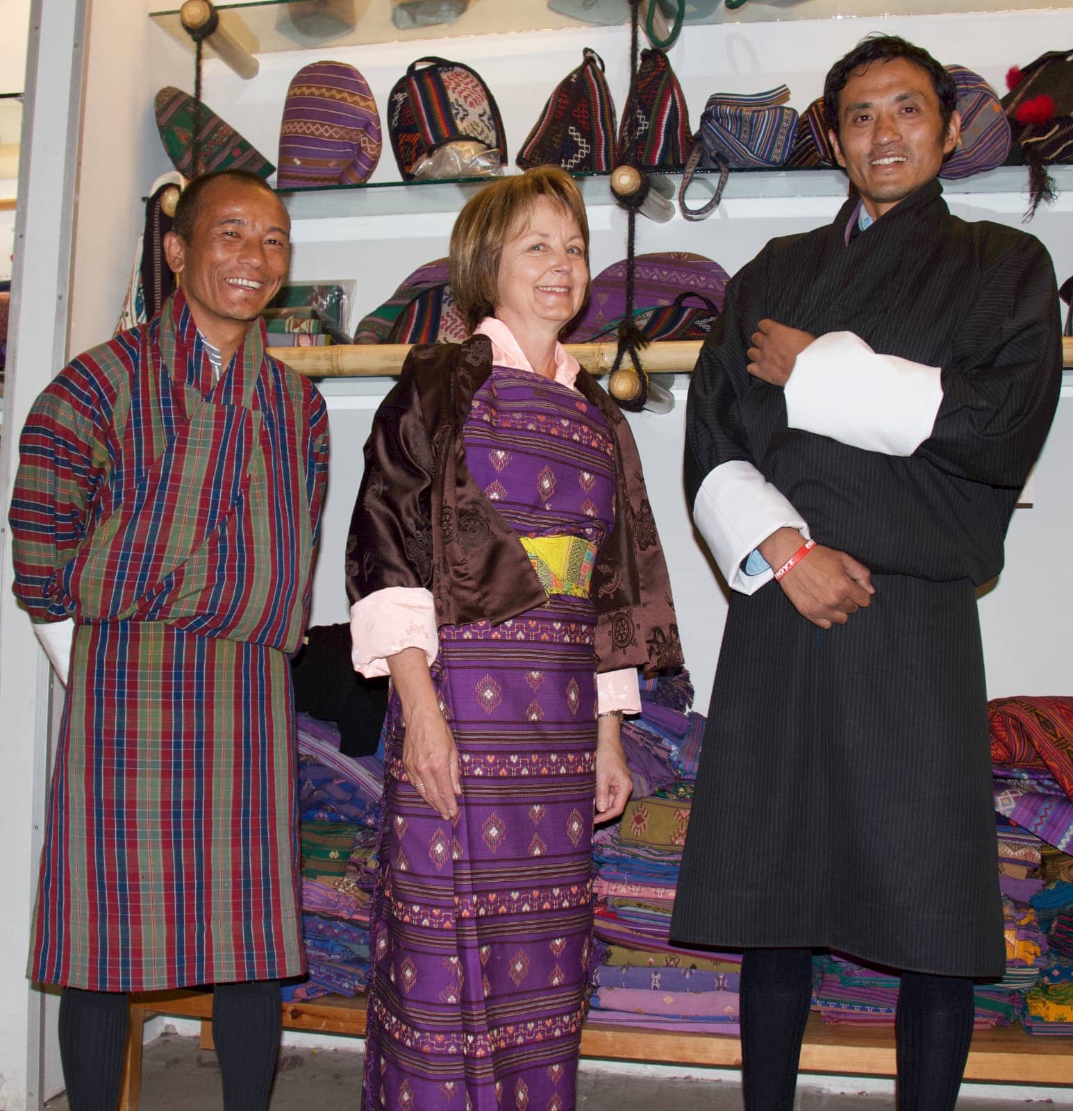 Two men and one woman smiling at camera dressed in Bhutanese clothing
