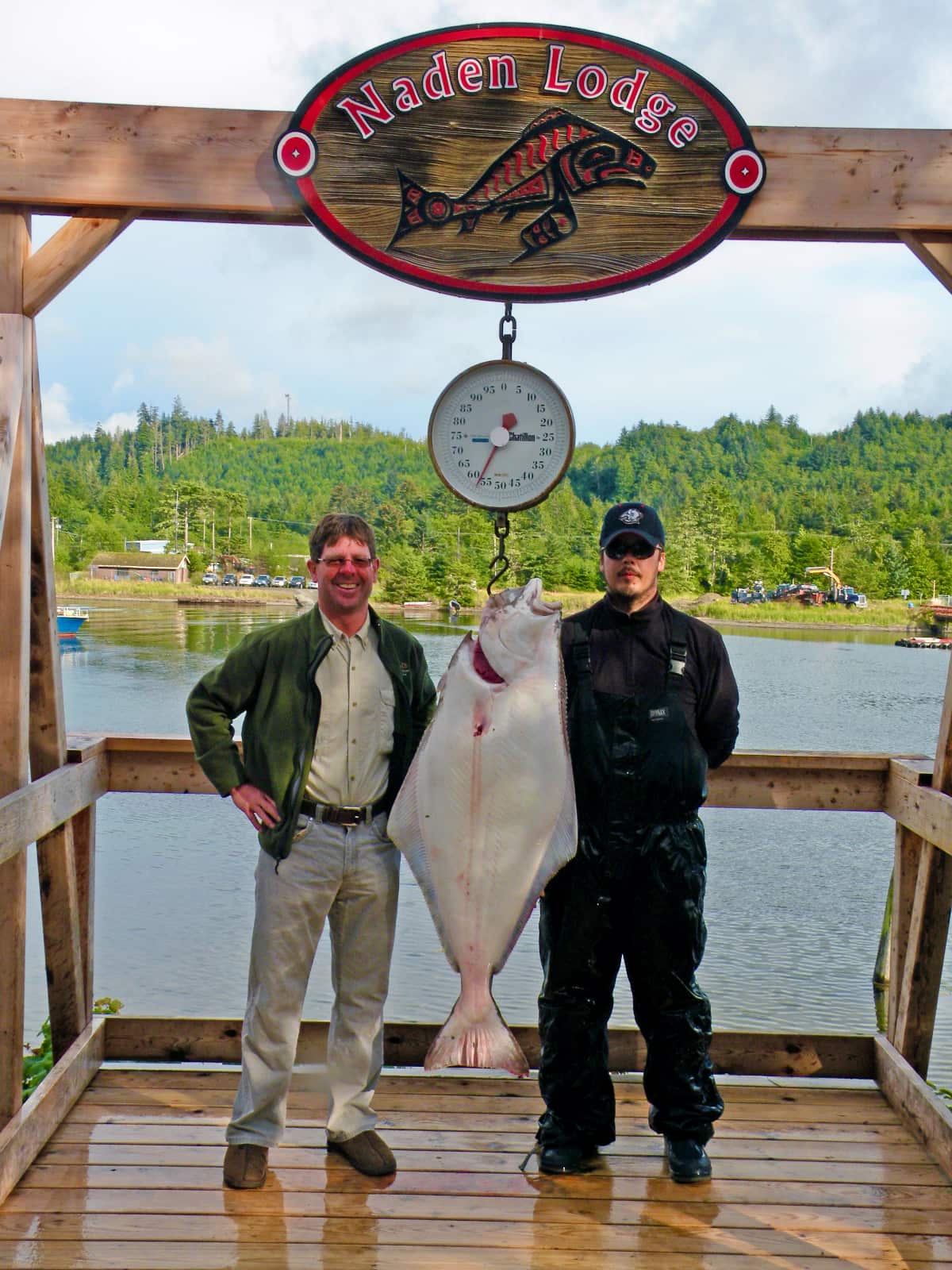 Two men posing with fish hanging on scale