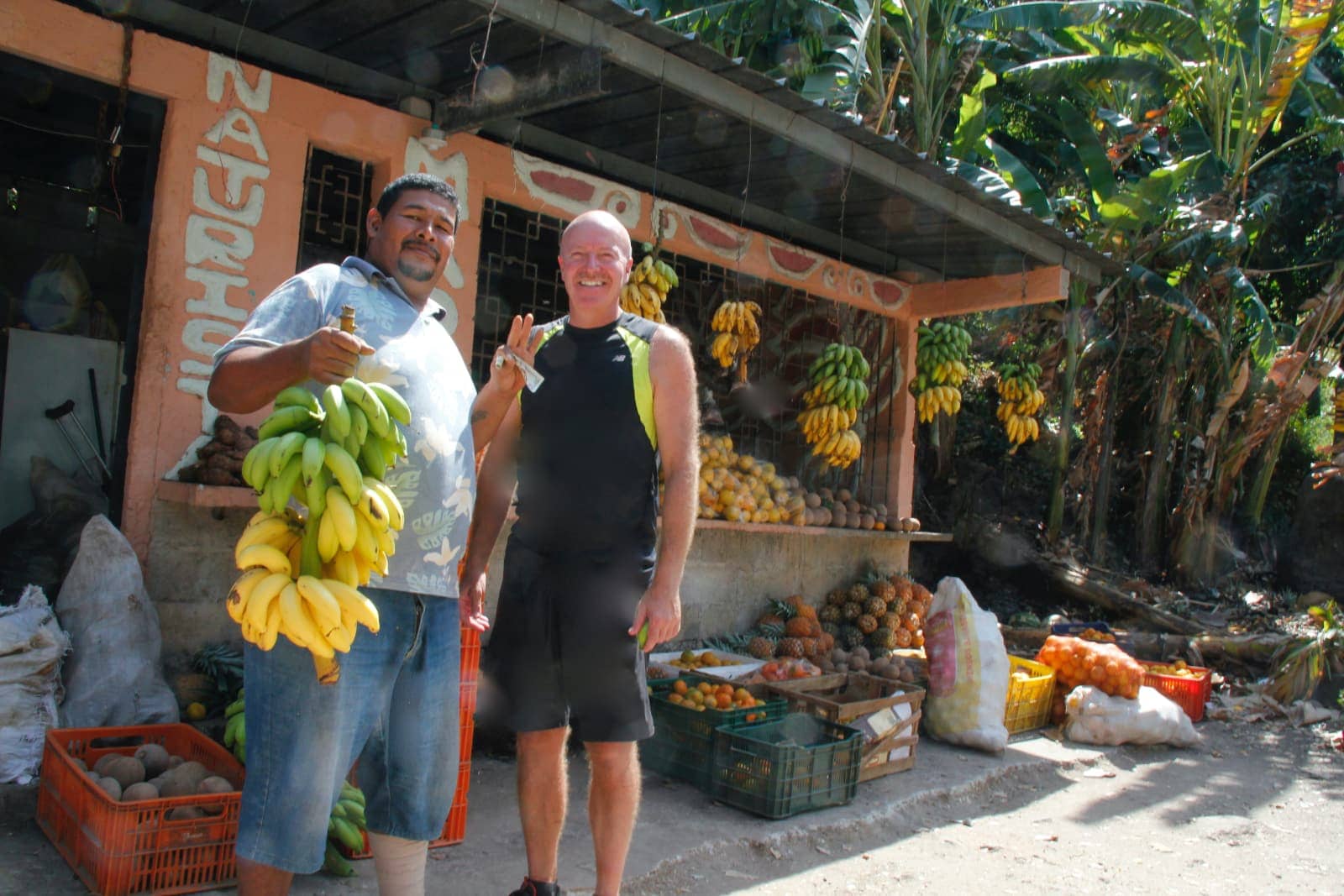 Two men smiling at fruit stand with bananas