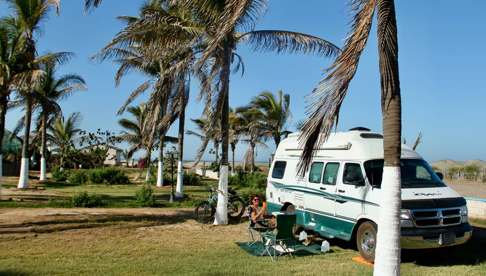 White and turquoise camper van and woman sitting in chair