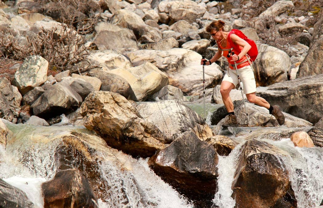 Woman hiking across boulders and running water