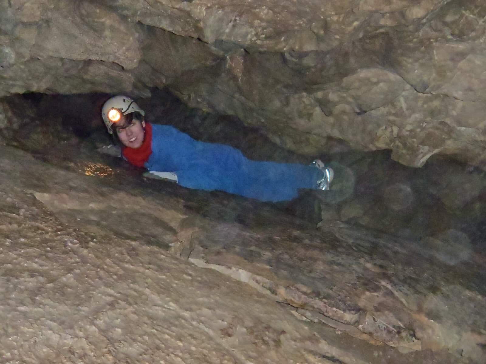 Woman in blue coveralls crawling through narrow cave