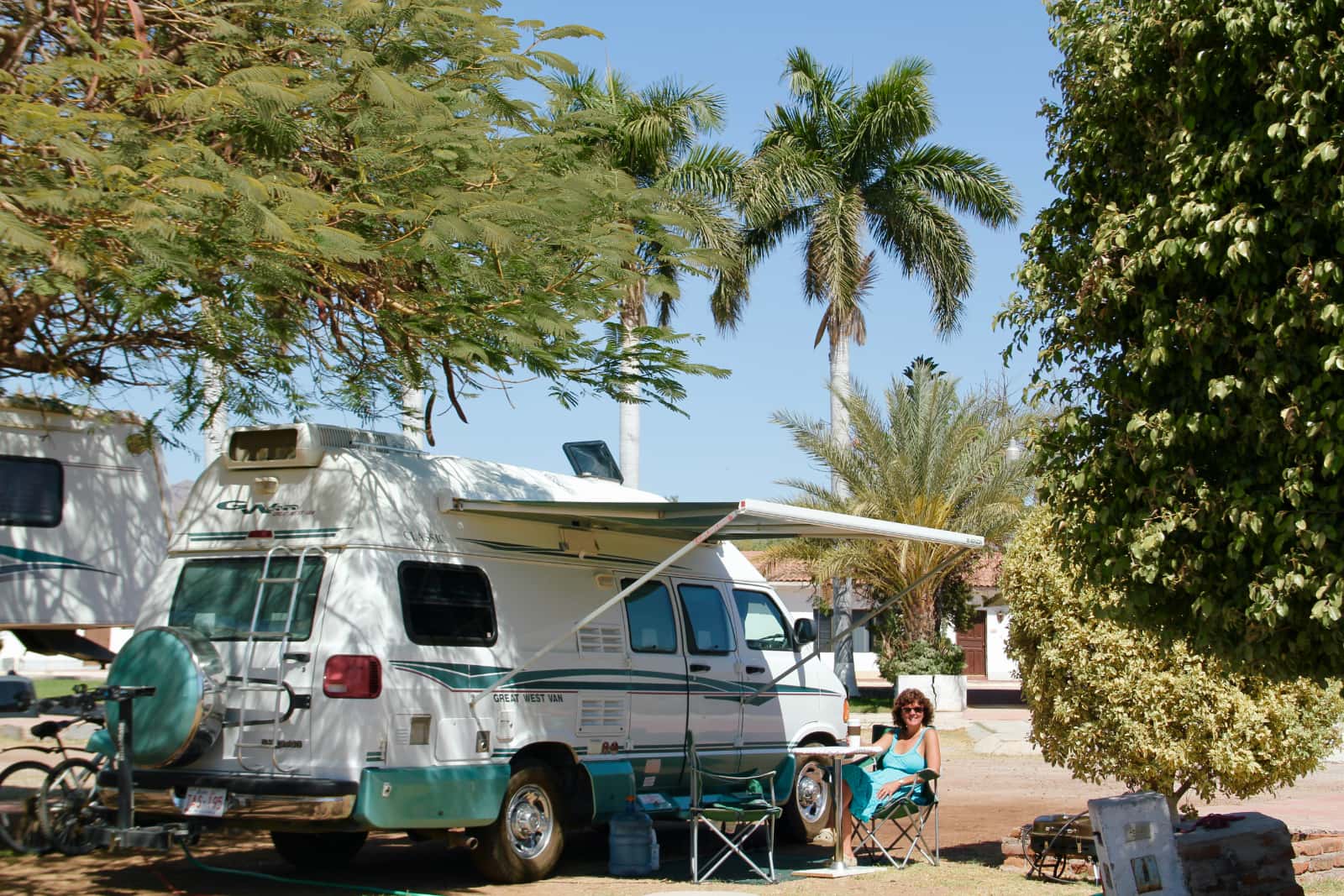 Woman in blue dress sitting next to white and turquoise camper van