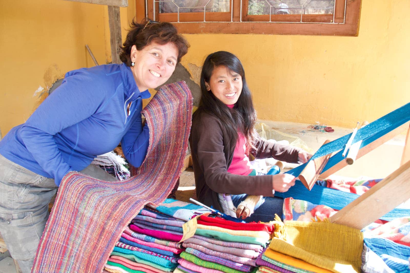 Woman in blue jacket admiring woven textiles from another woman