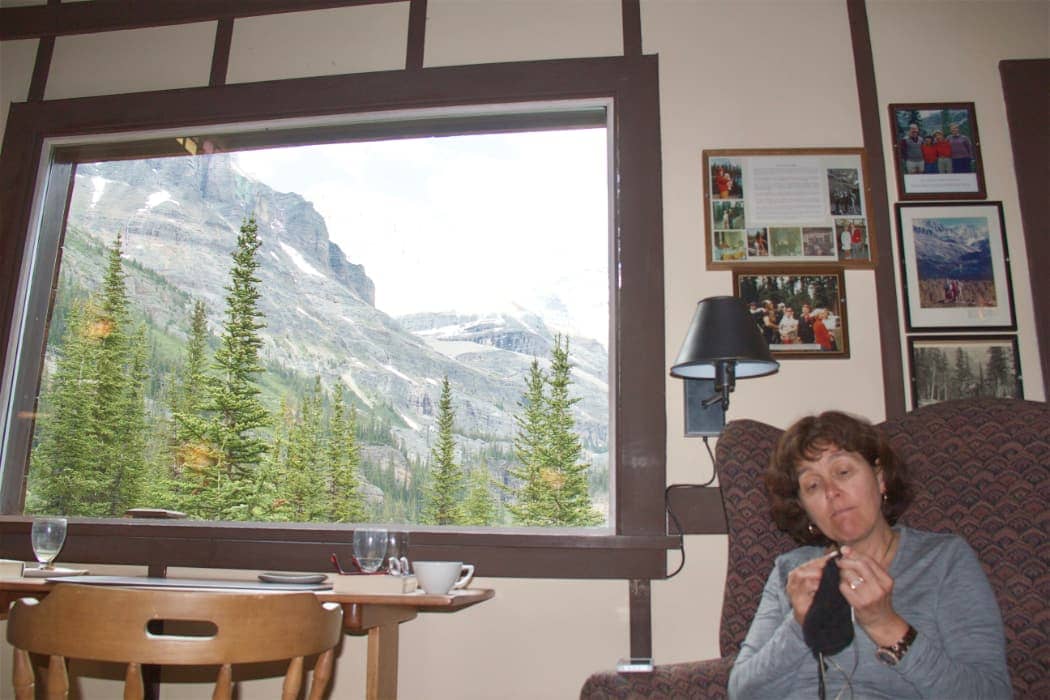 Woman knitting with window showing mountains in background