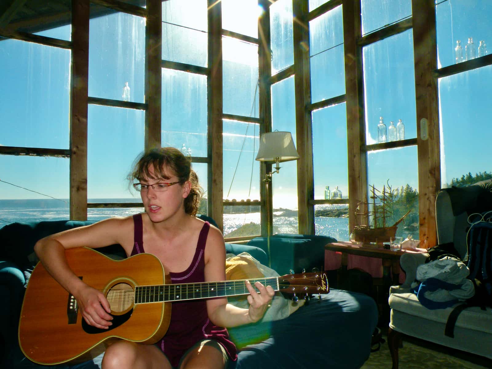 Woman playing guitar in foreground with ocean in background