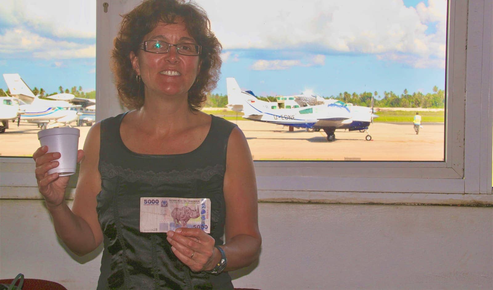 Woman posing with local currency in foreground with plane in background