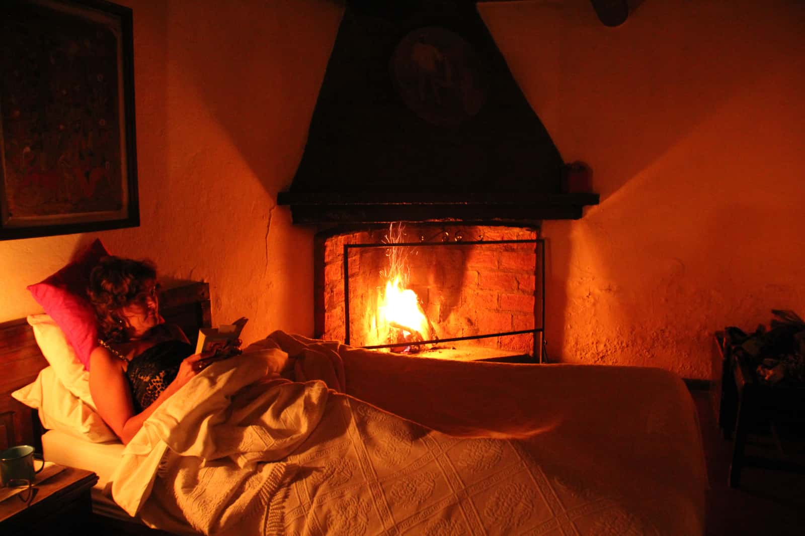 Woman reading in bed with fireplace in background