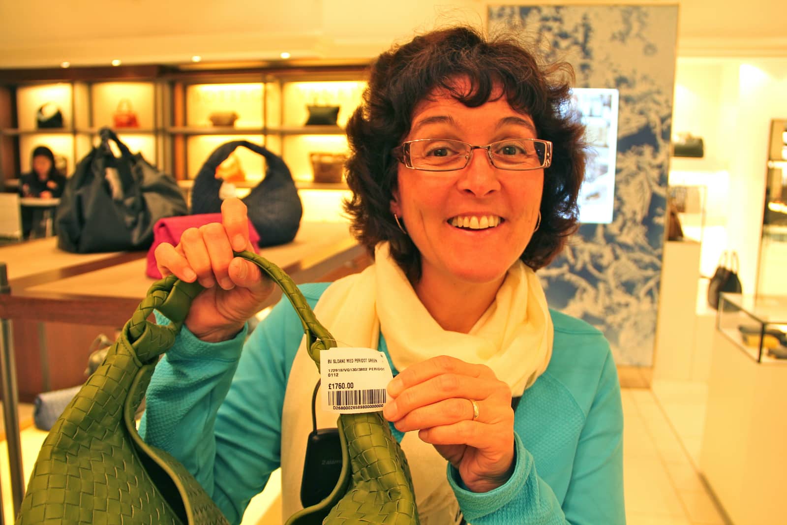 Woman showing price of handbag with other handbags in background