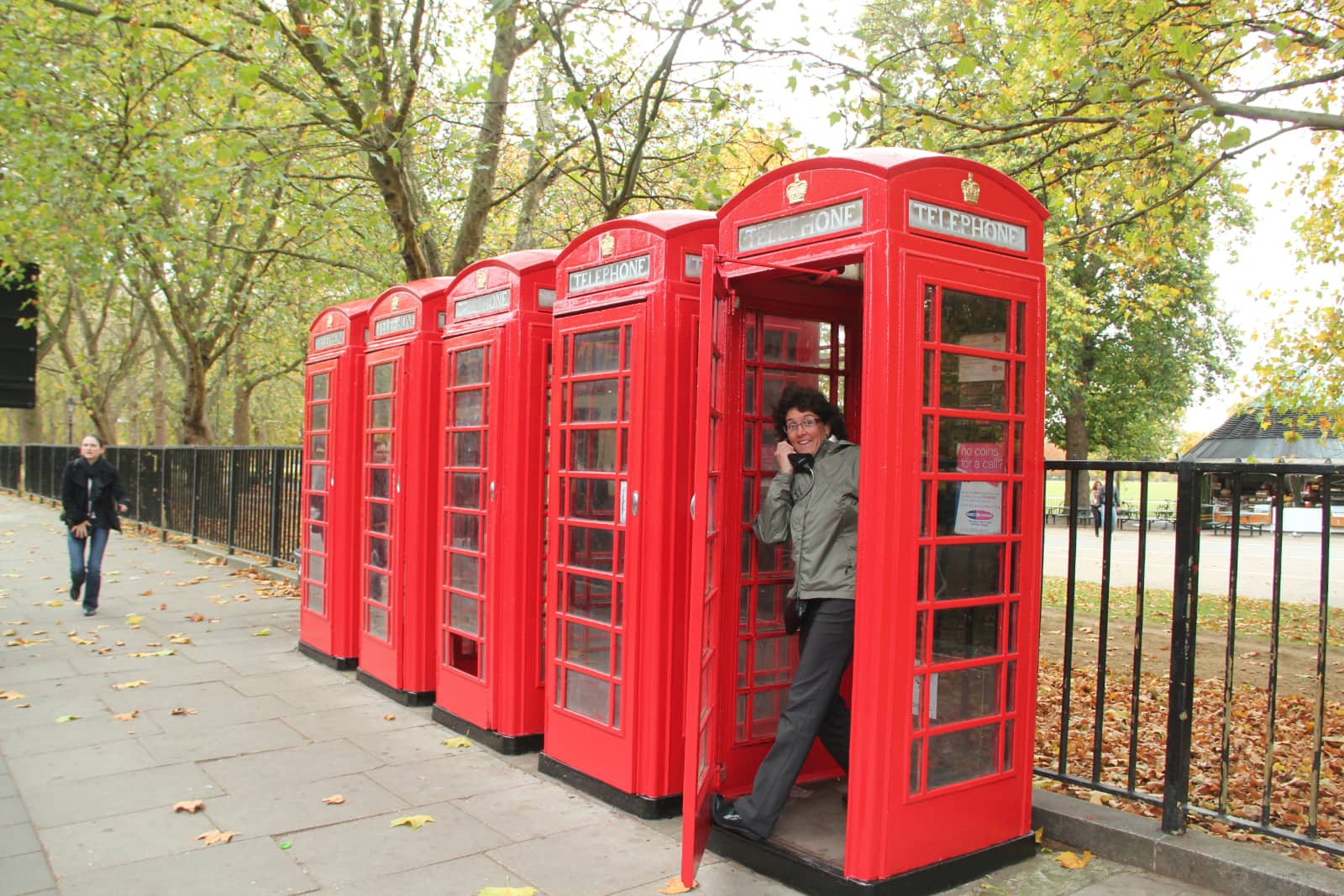 Woman standing in iconic red phone booth with single woman walking in background