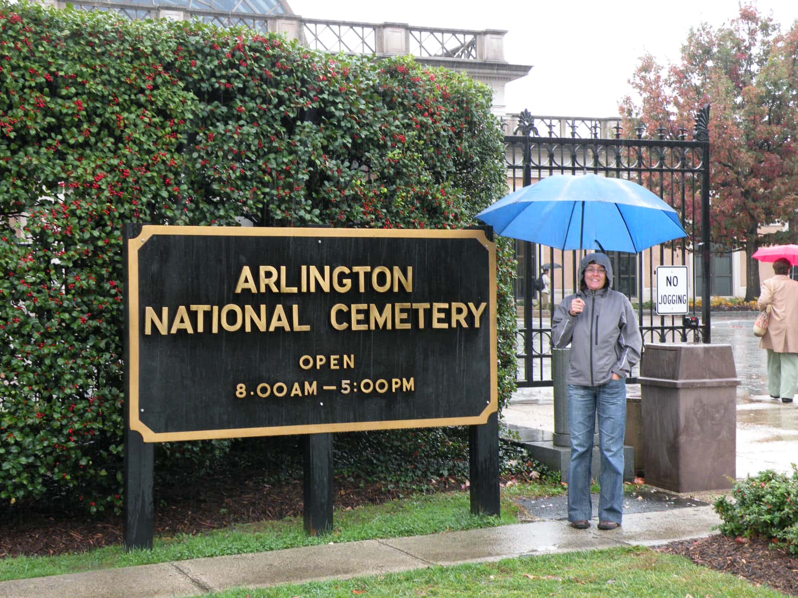 Woman standing with blue umbrella next to Arlington National cemetery sign