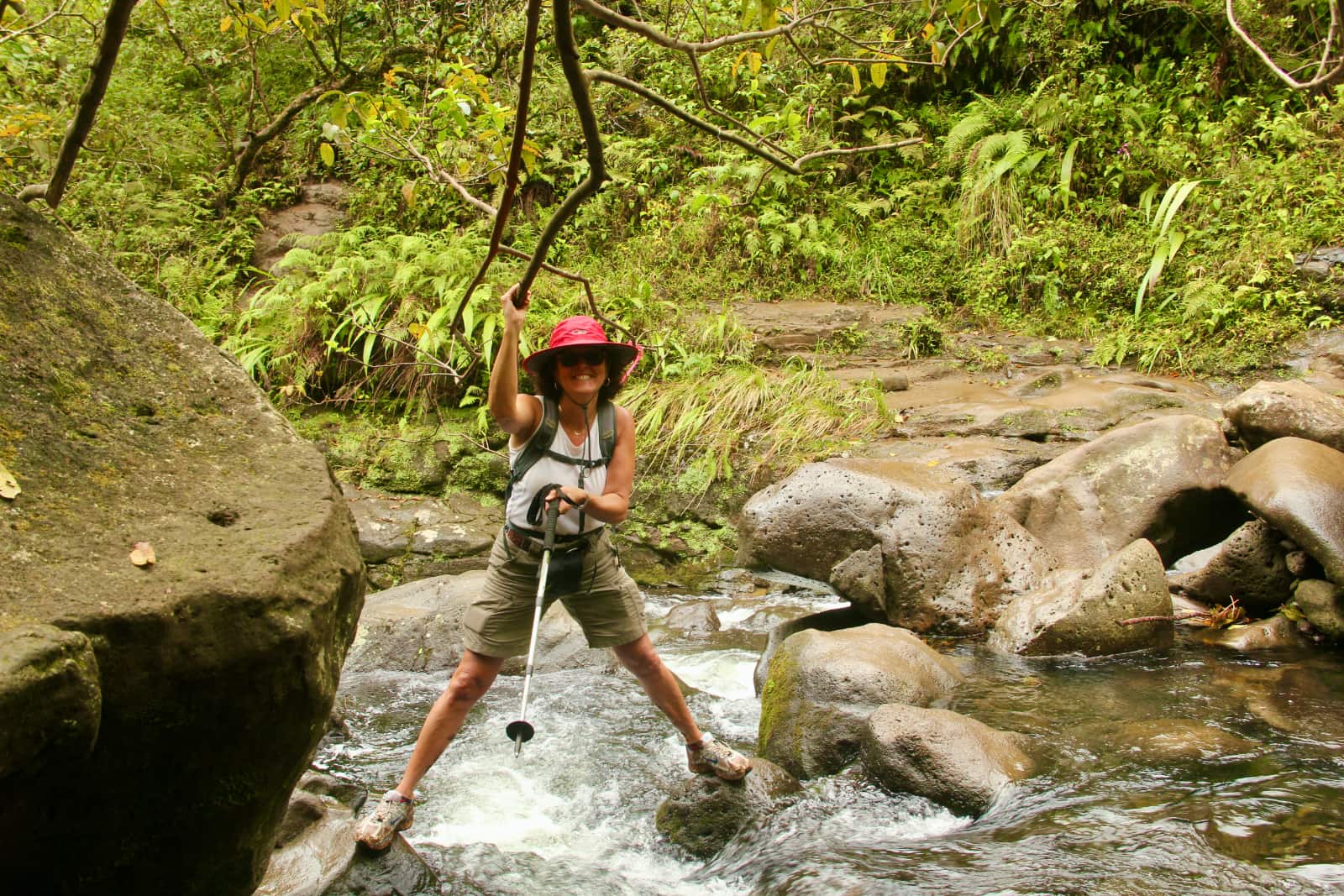 Woman with red hat crossing river in rainforest