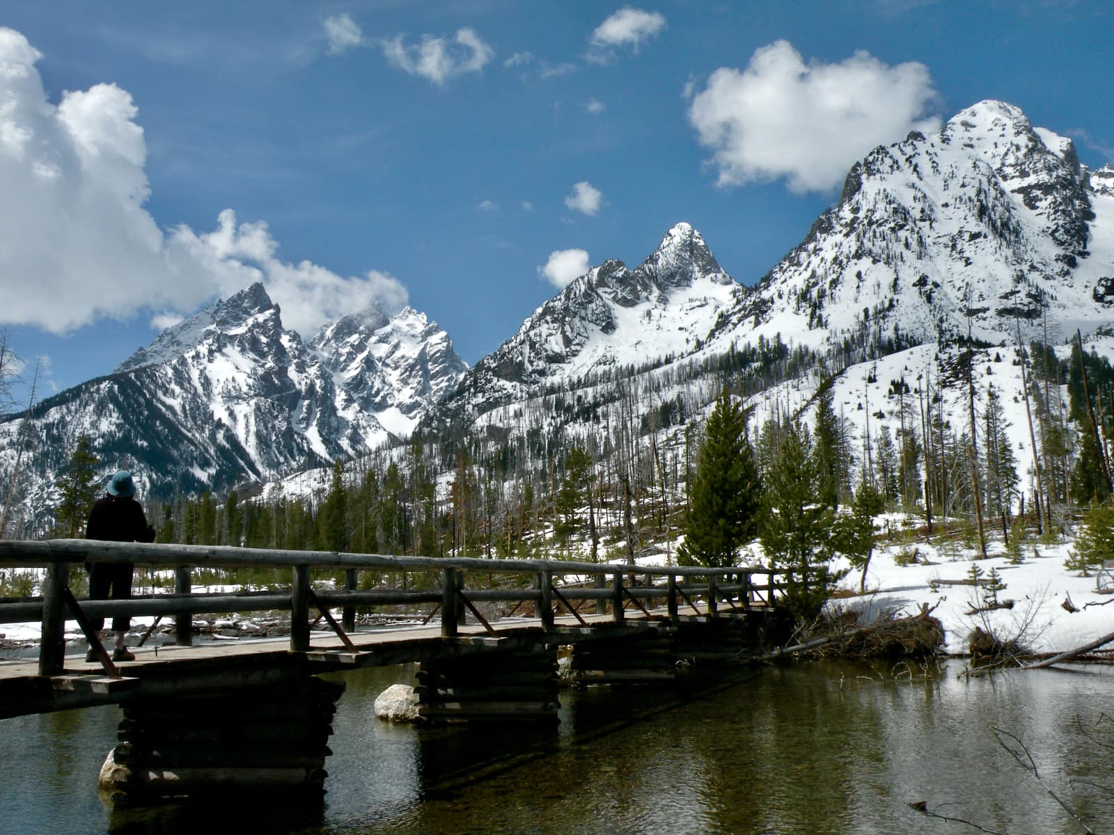 Wooden bridge over river in foreground with snow covered mountains in background