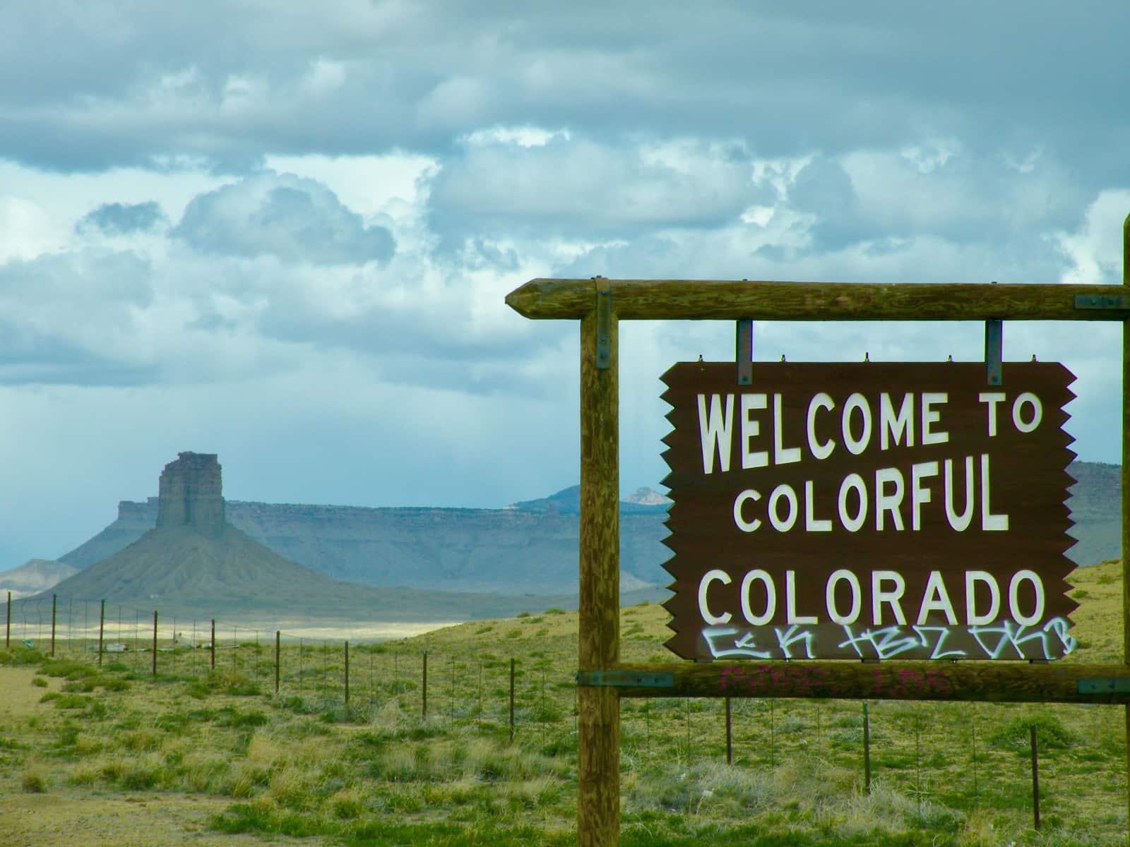 Wooden sign with welcome to Colorado text in foreground with mountains in background