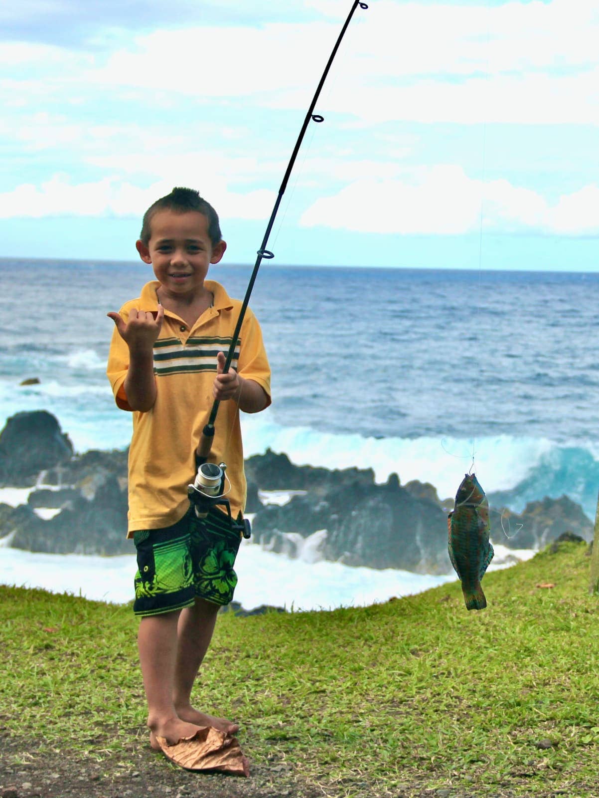 Young boy posing with fish and fishing rod with ocean waves-in background