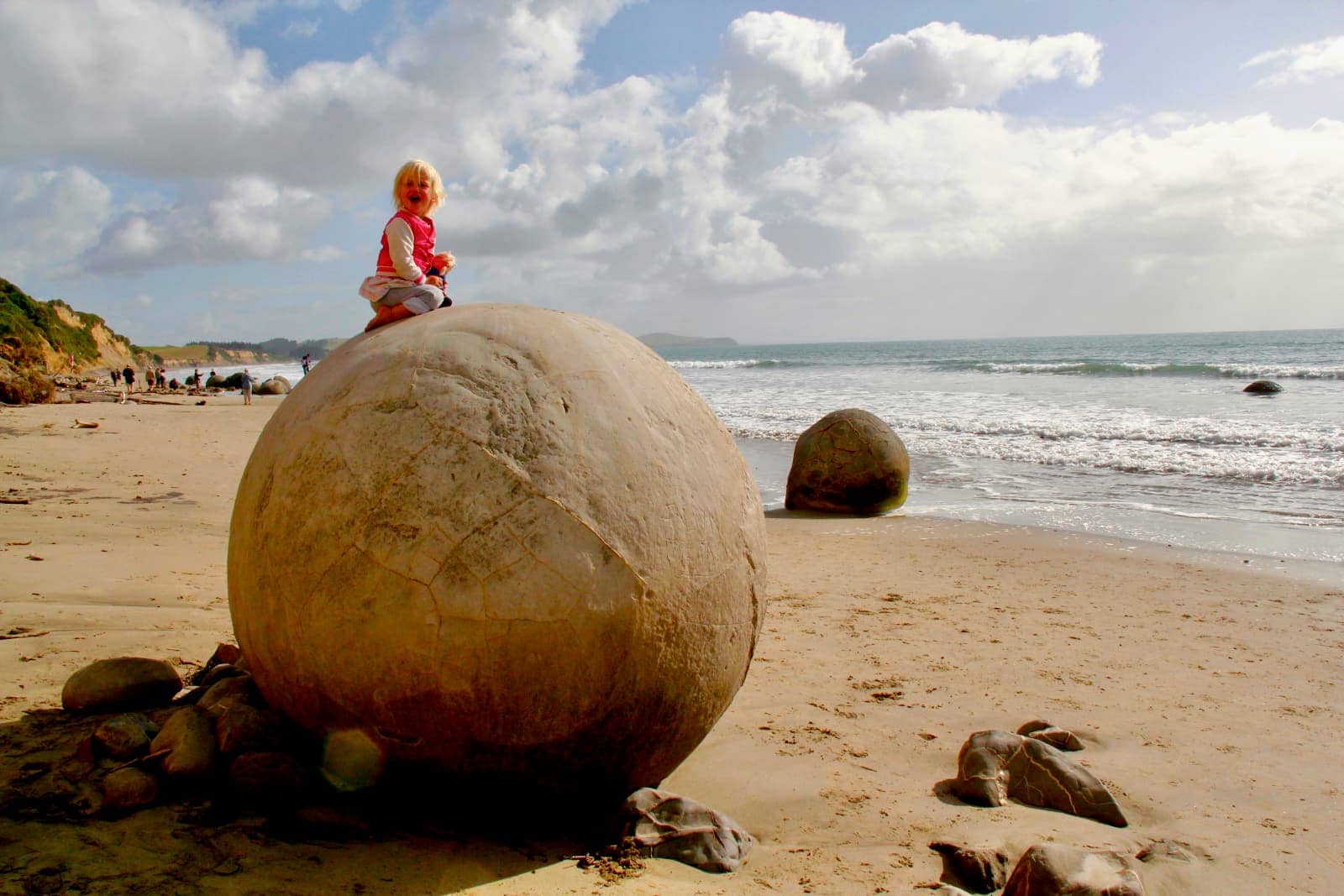 Young girl in pink vest sitting on large spherical boulder