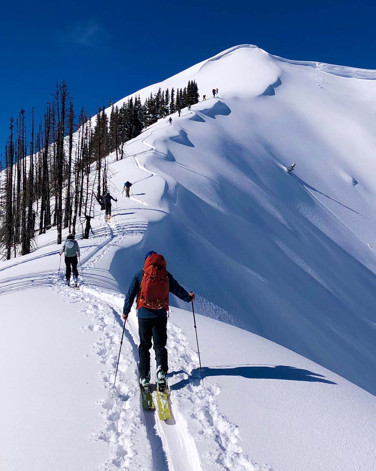 Skiers climb snowy mountain ridge
