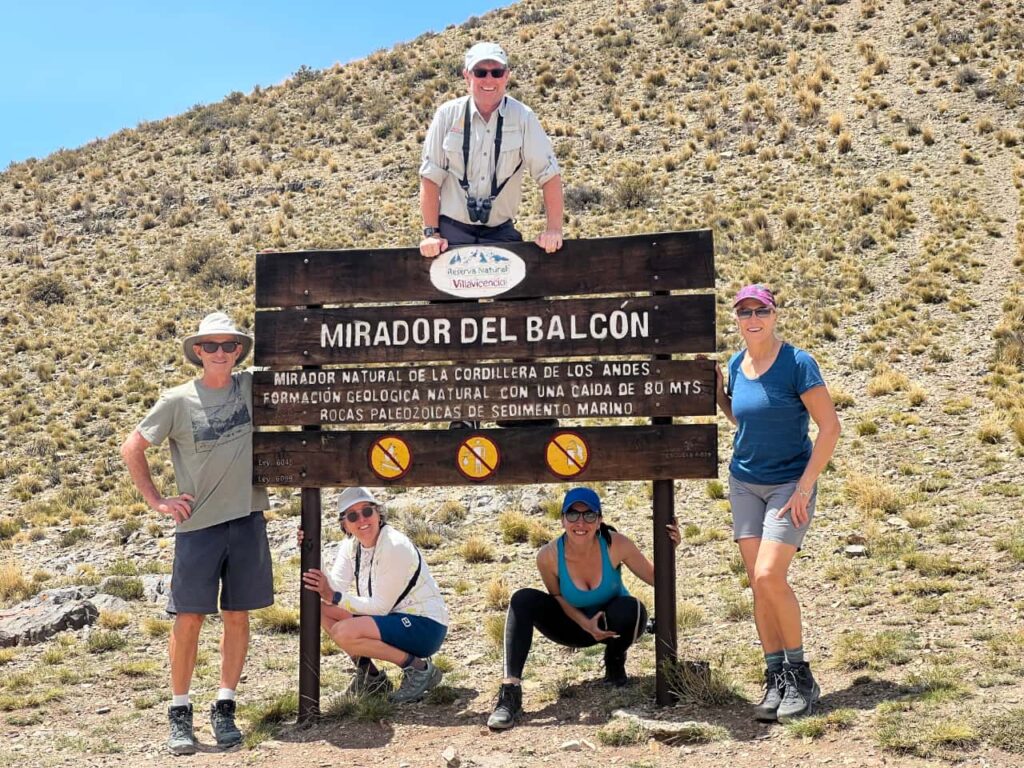 Group of hikers standing beside sign with dry hill in background