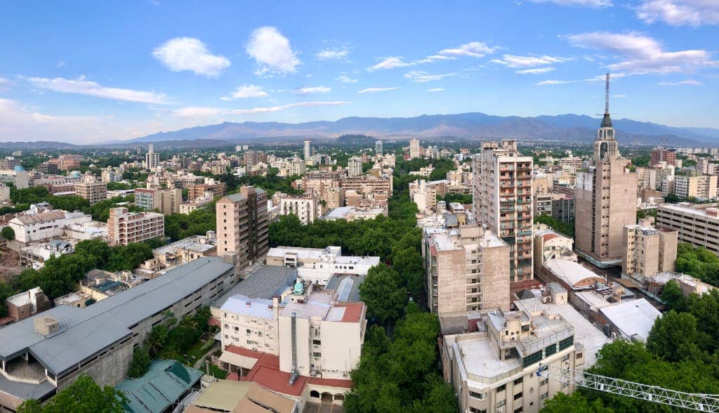 View of multiple buildings and trees with mountains and blue sky in the background