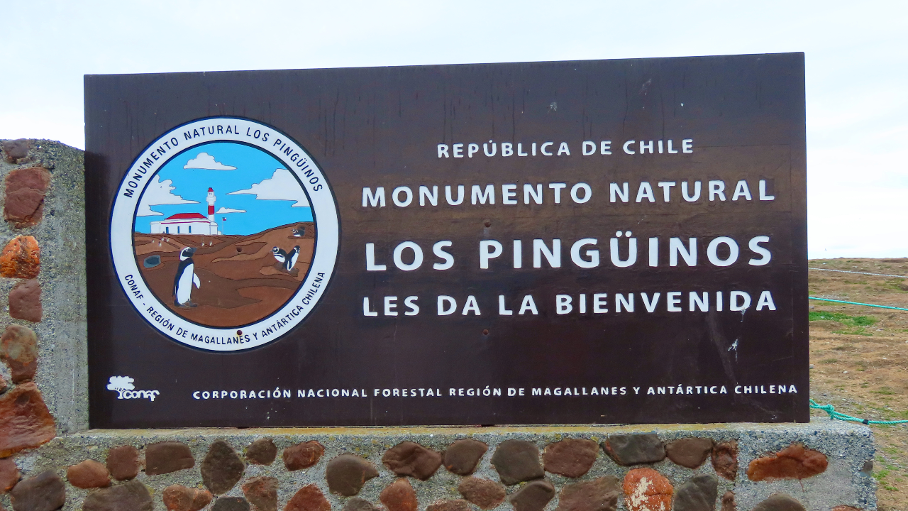 A sign reading "Republica de Chile, Monumento Natural, Los Pinguinos, Les Da La Beinvenida".