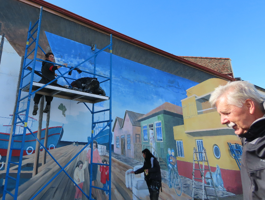 Street art depicting colourful buildings on the right, and a blue boat on the left.