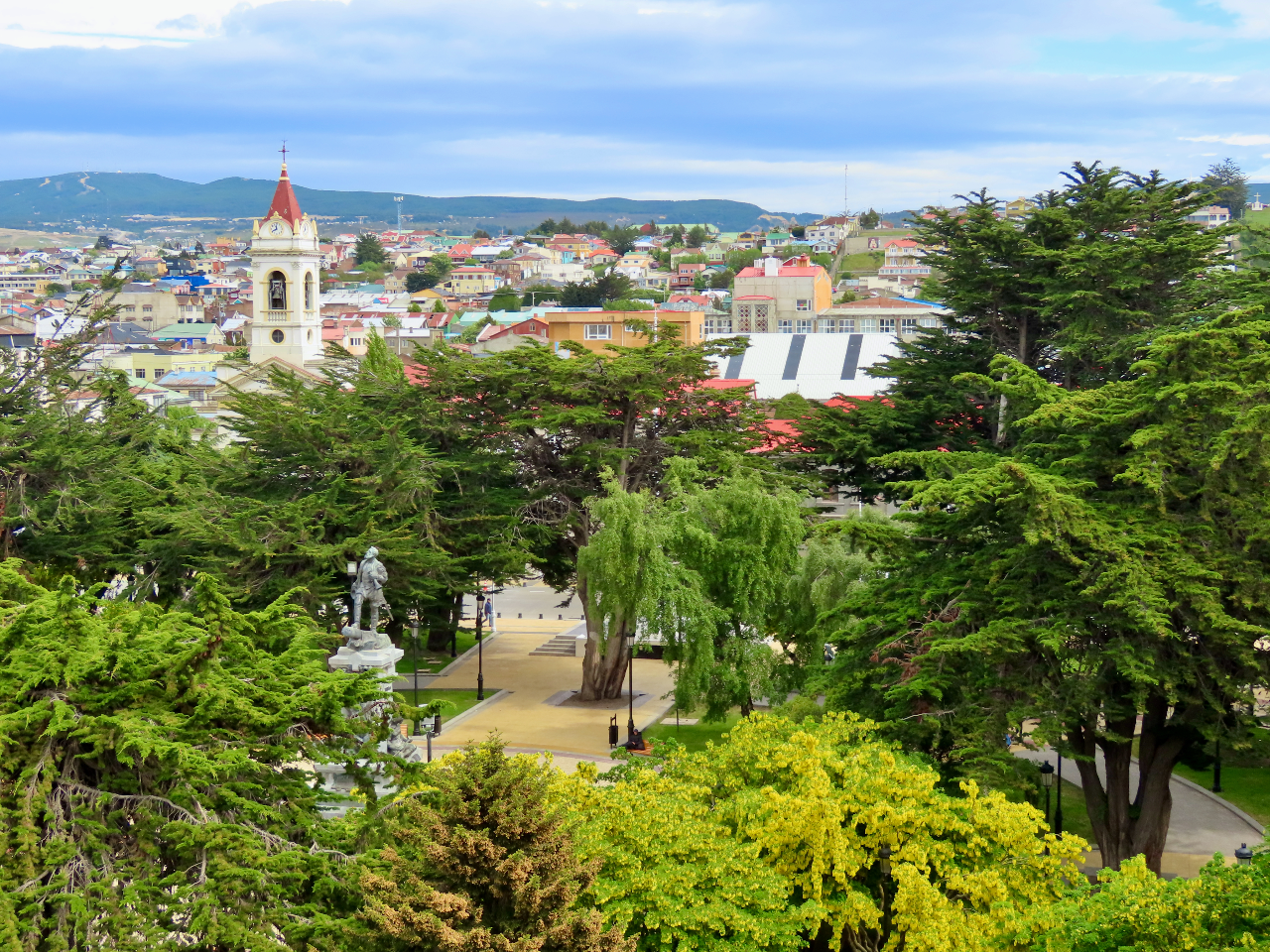 Luscious green trees in the foreground with colourful buildings in the background.