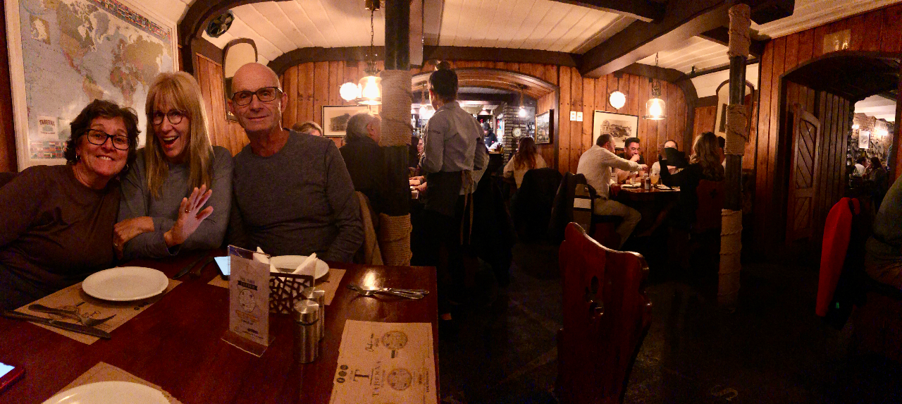 A group of three people smile and wave for the camera in a wood paneled restaurant.